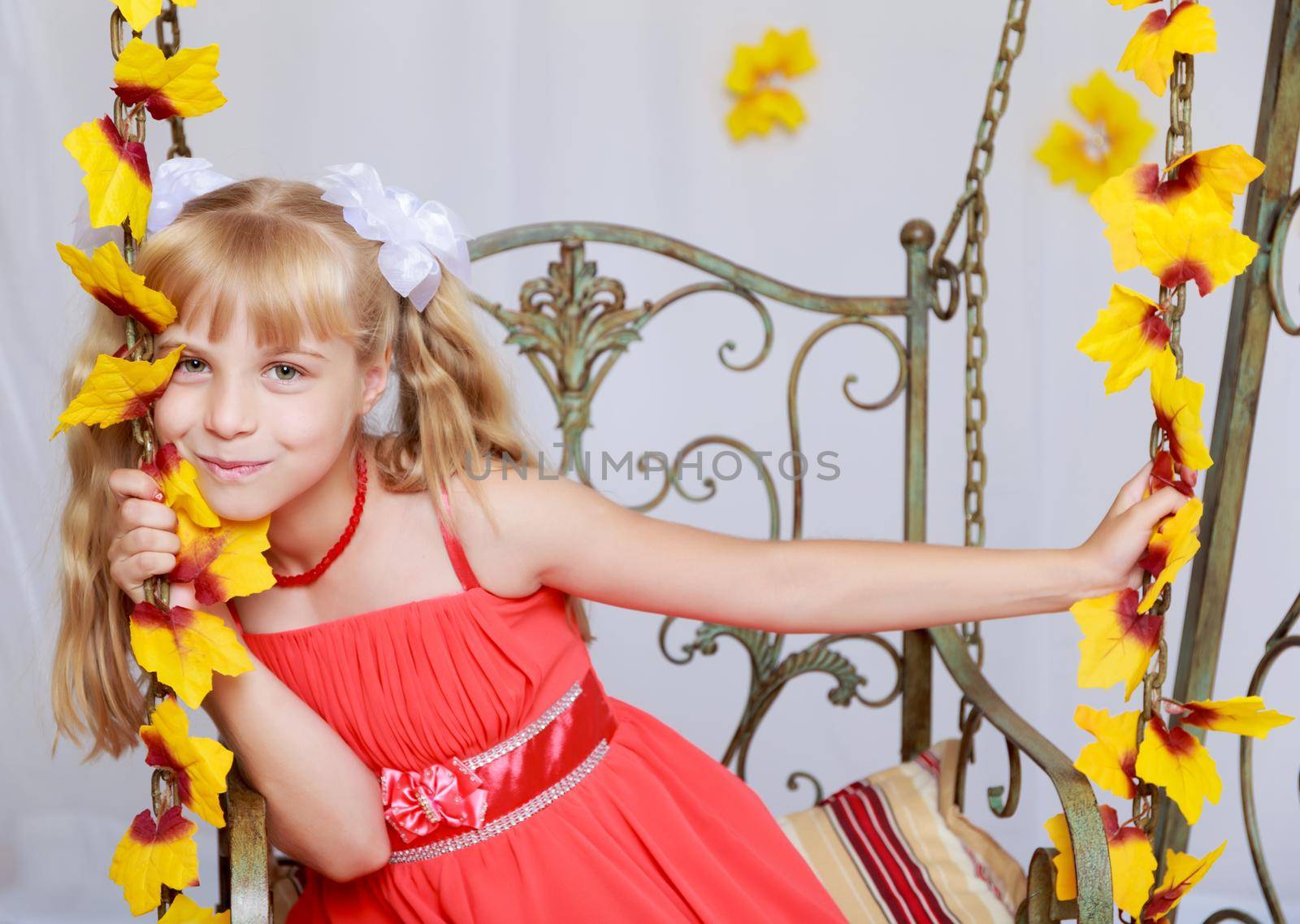 Dreaming little girl in red long dress on a swing decorated with yellow flowers. Dream close-up