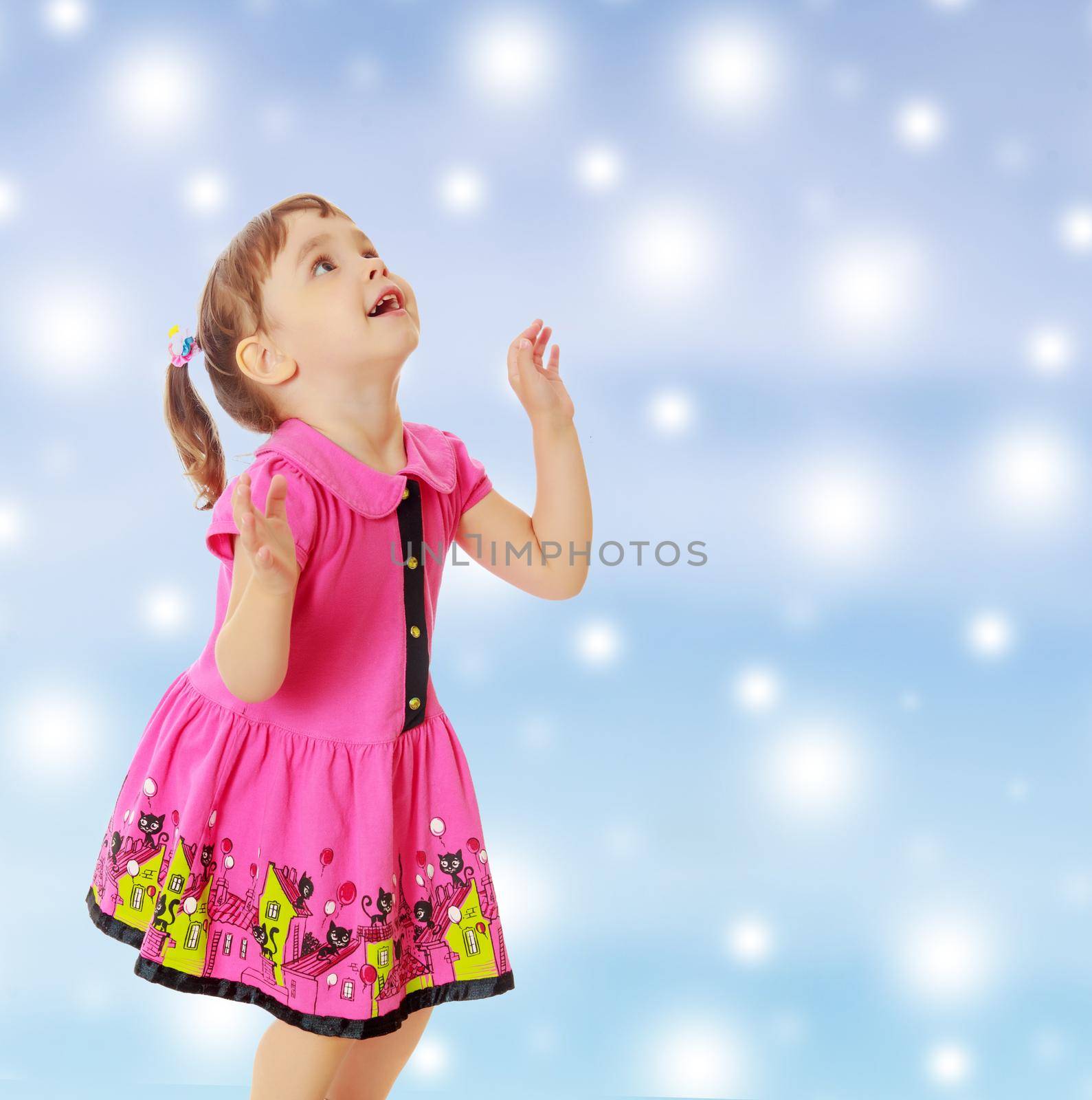 Pensive little girl with pigtails on the head , in a pink dress. The girl was looking at the top turned sideways to the camera.On new year or Christmas blue background with white big stars.