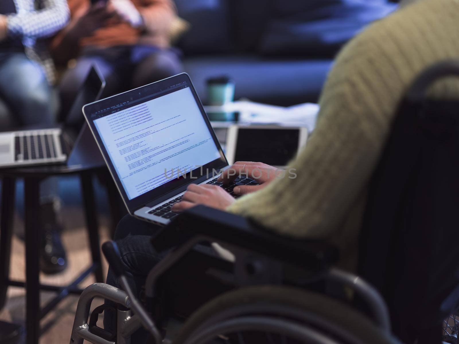 Closeup of a woman in a wheelchair working on a laptop computer at the office. Concept inclusion of disabled people in business. Business team meeting in background. High quality photo