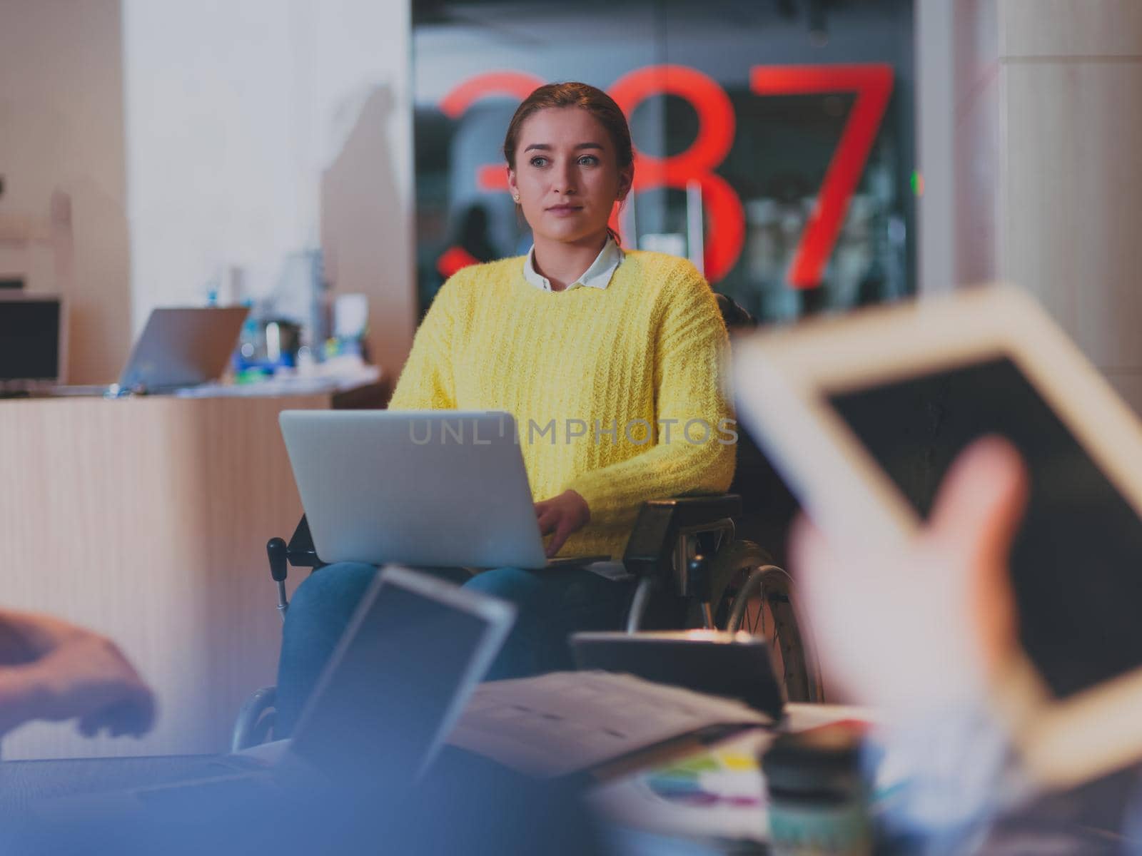 Handicapped businesswoman in a wheelchair on meeting with her diverse business team brainstorming about ideas and plans in a modern open space coworking office space. High quality photo