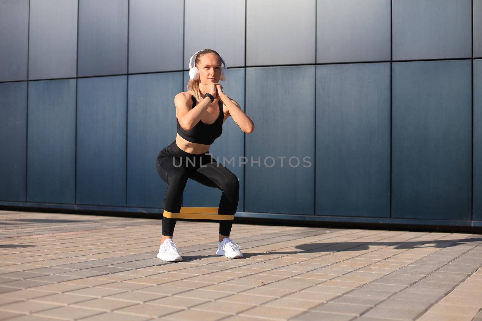 Sporty woman doing squats with fitness gum expander outdoors