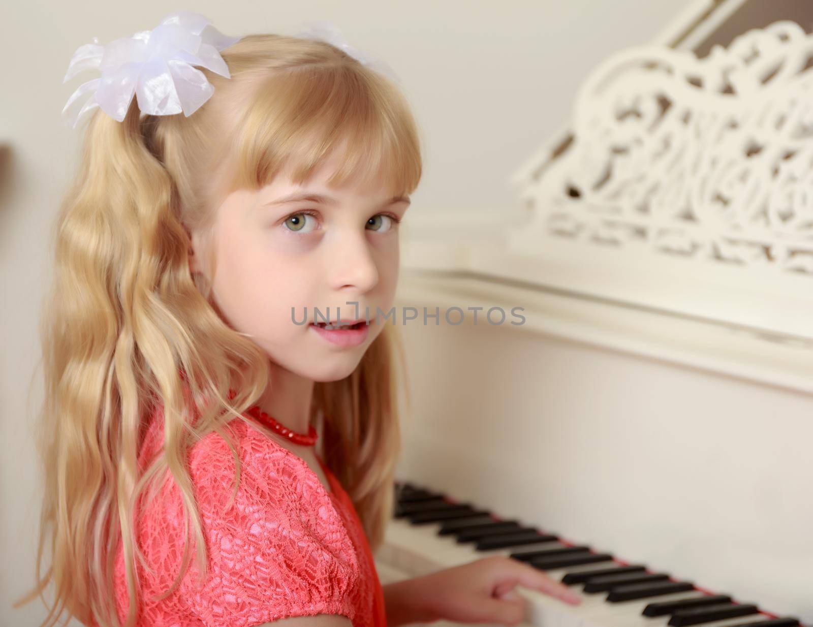 Beautiful little girl in a long orange dress,with long blond hair braided in ponytails , playing the piano . Close-up