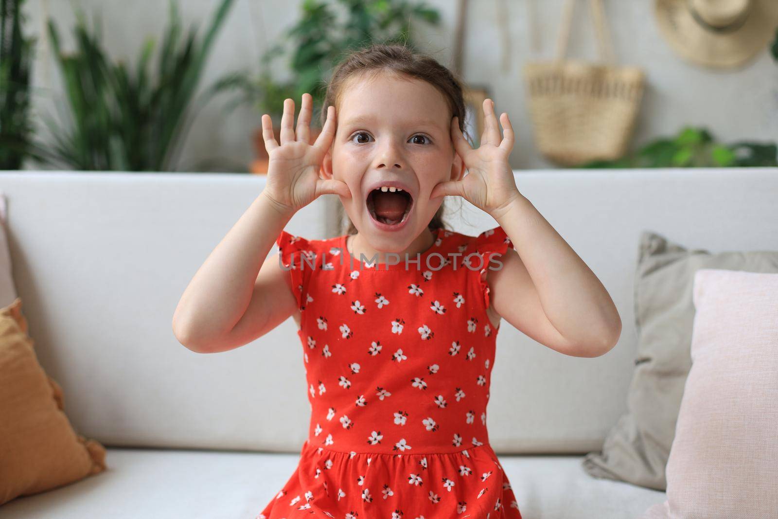 Adorable little girl making faces while sitting on sofa ta living room