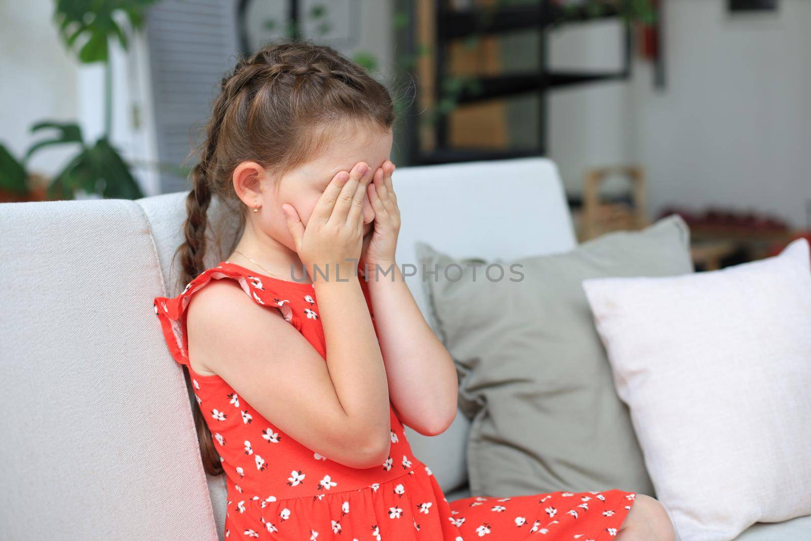 Sad little girl sitting on sofa alone at home. by tsyhun