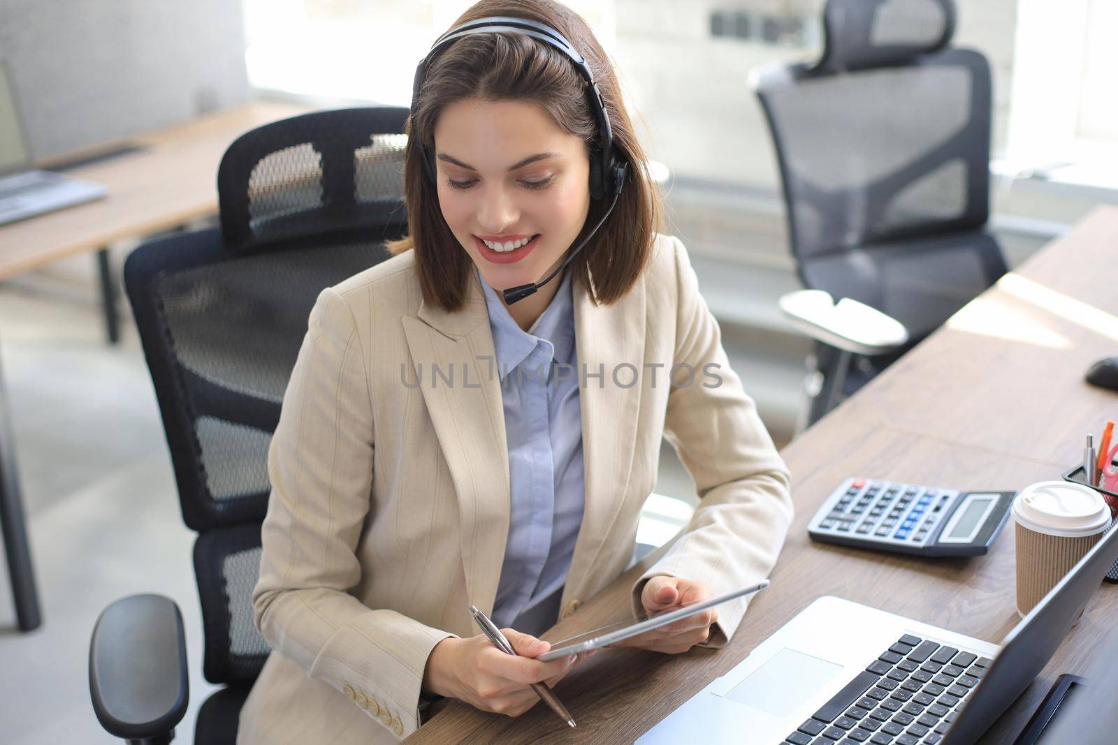 Cheerful female manager sitting at office desk and performing corporate tasks using wireless connection on digital gadgets. by tsyhun