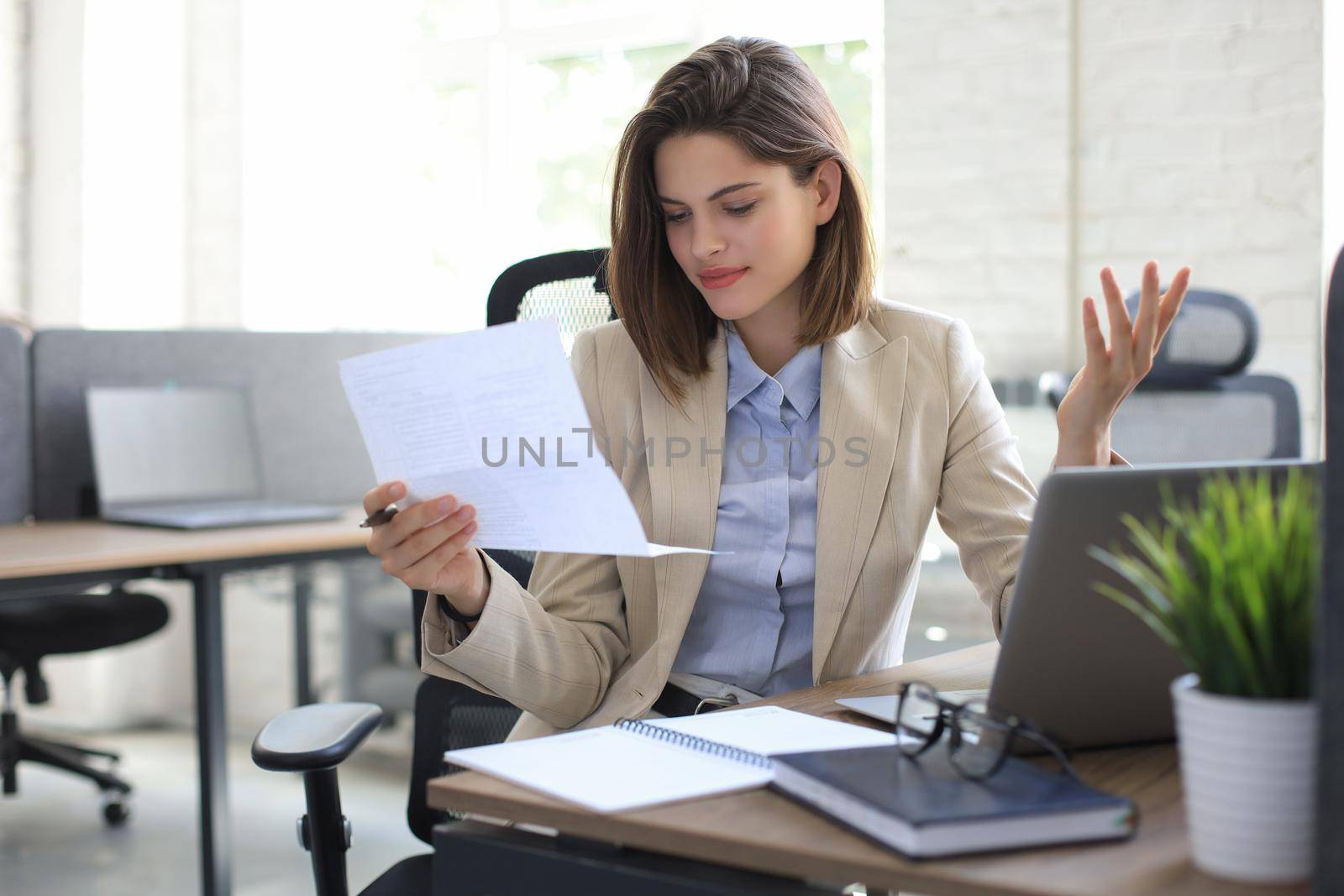 Attractive cheerful business woman checking paper documents in office, working on laptop