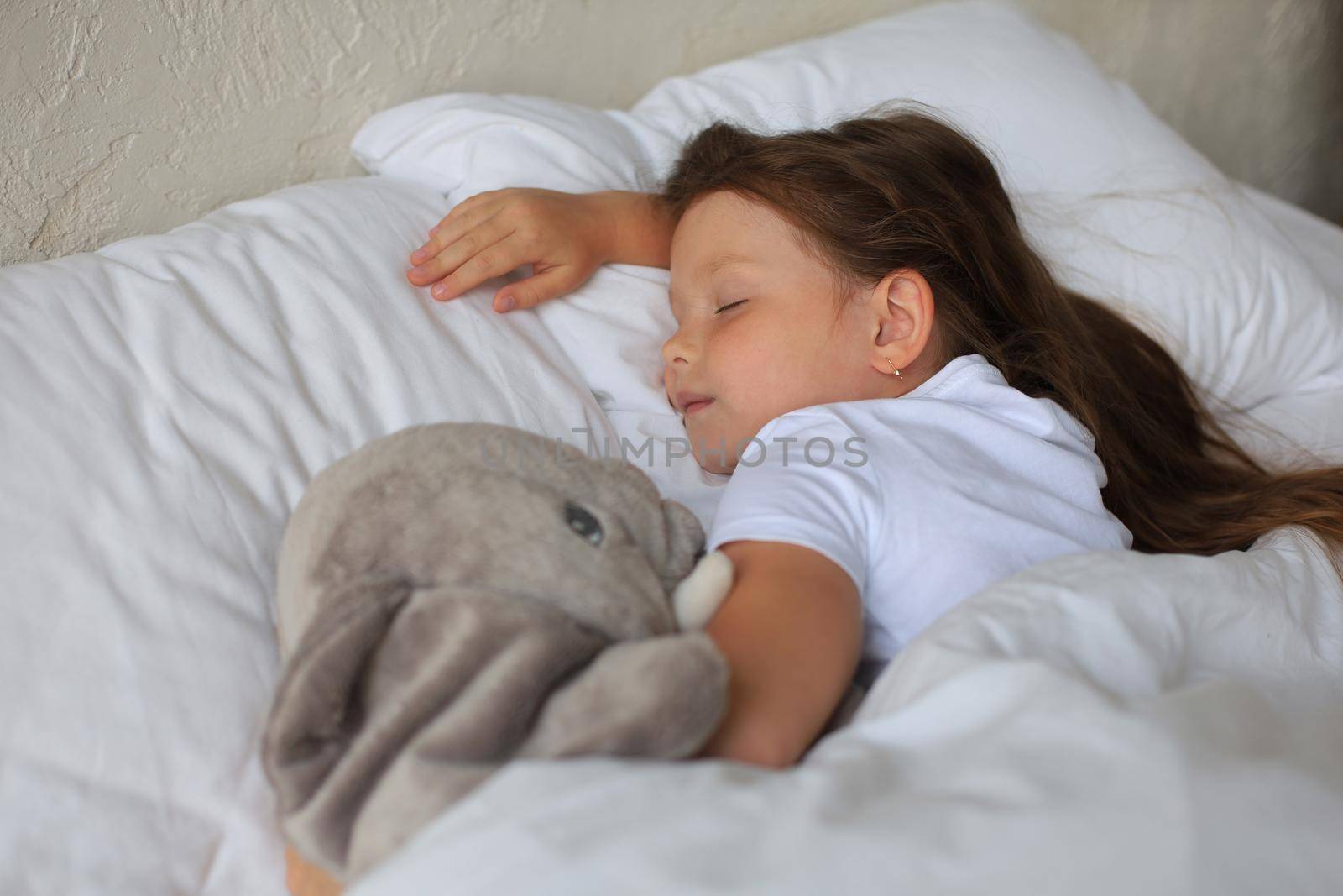 Cute child little girl sleeps in the bed with a toy elephant