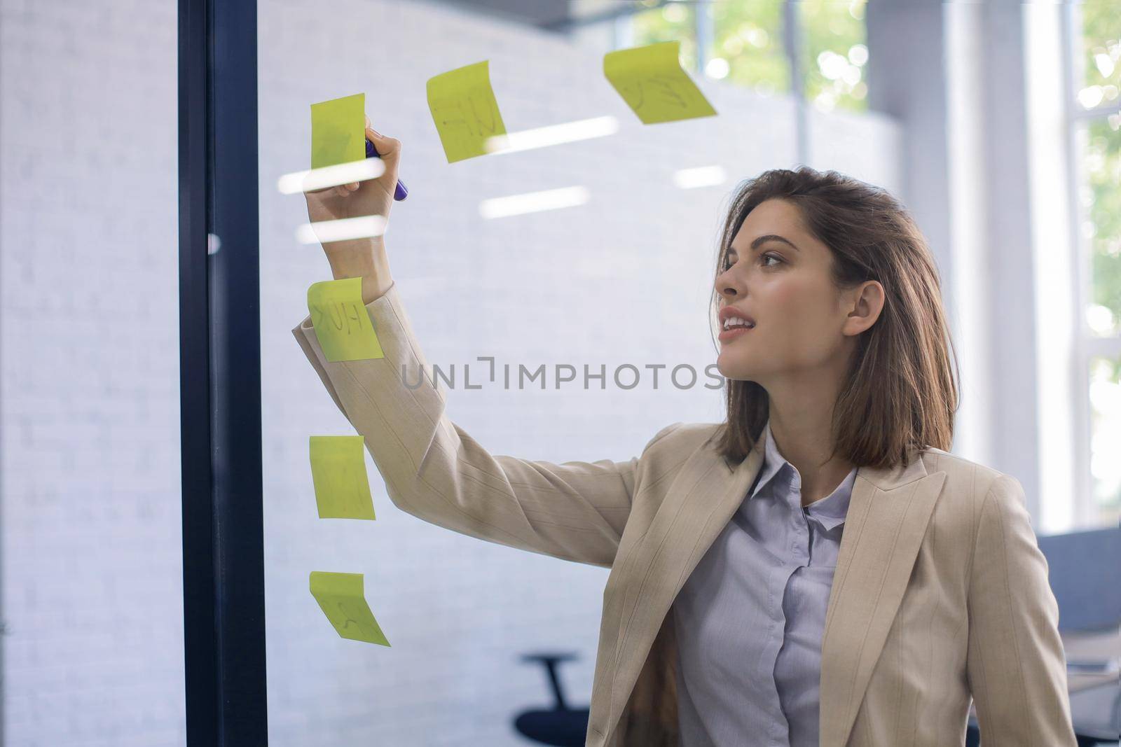 Attractive busness woman post stickers on glass at office and writing on them