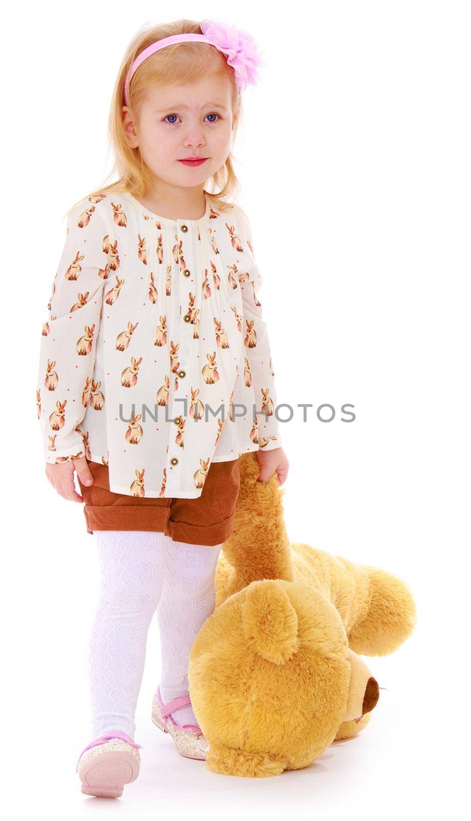 Cute little Caucasian girl in a white tank top and shorts , holds the paw of a Teddy bear - Isolated on white background