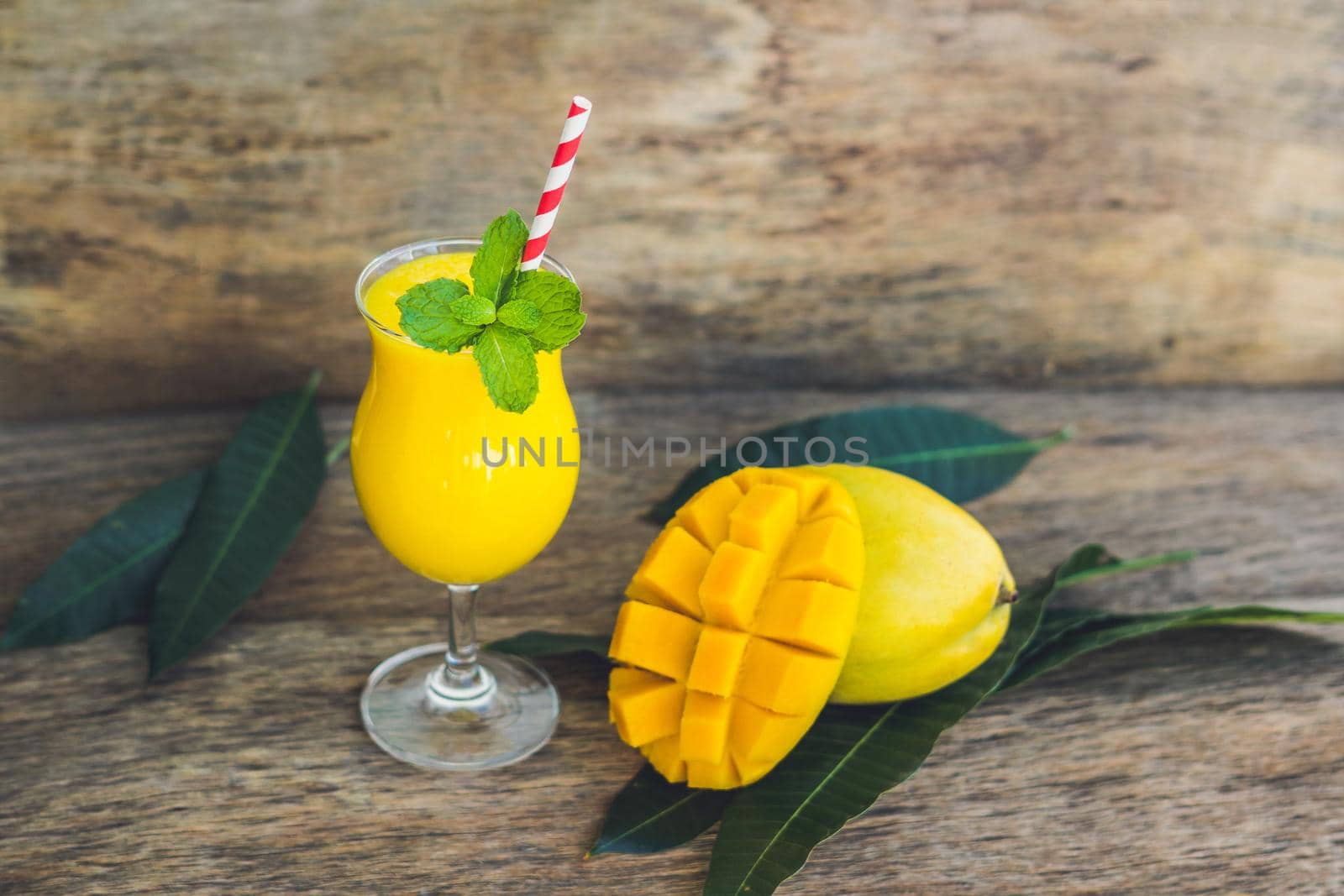 Juicy smoothie from mango in glass with striped red straw and with a mint leaf on old wooden background. Healthy life concept, copy space.