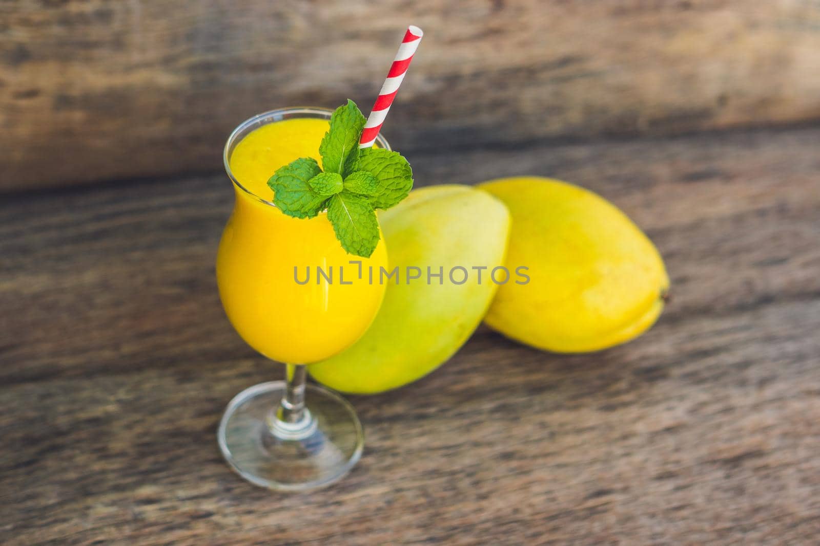 Juicy smoothie from mango in glass with striped red straw and with a mint leaf on old wooden background. Healthy life concept, copy space.