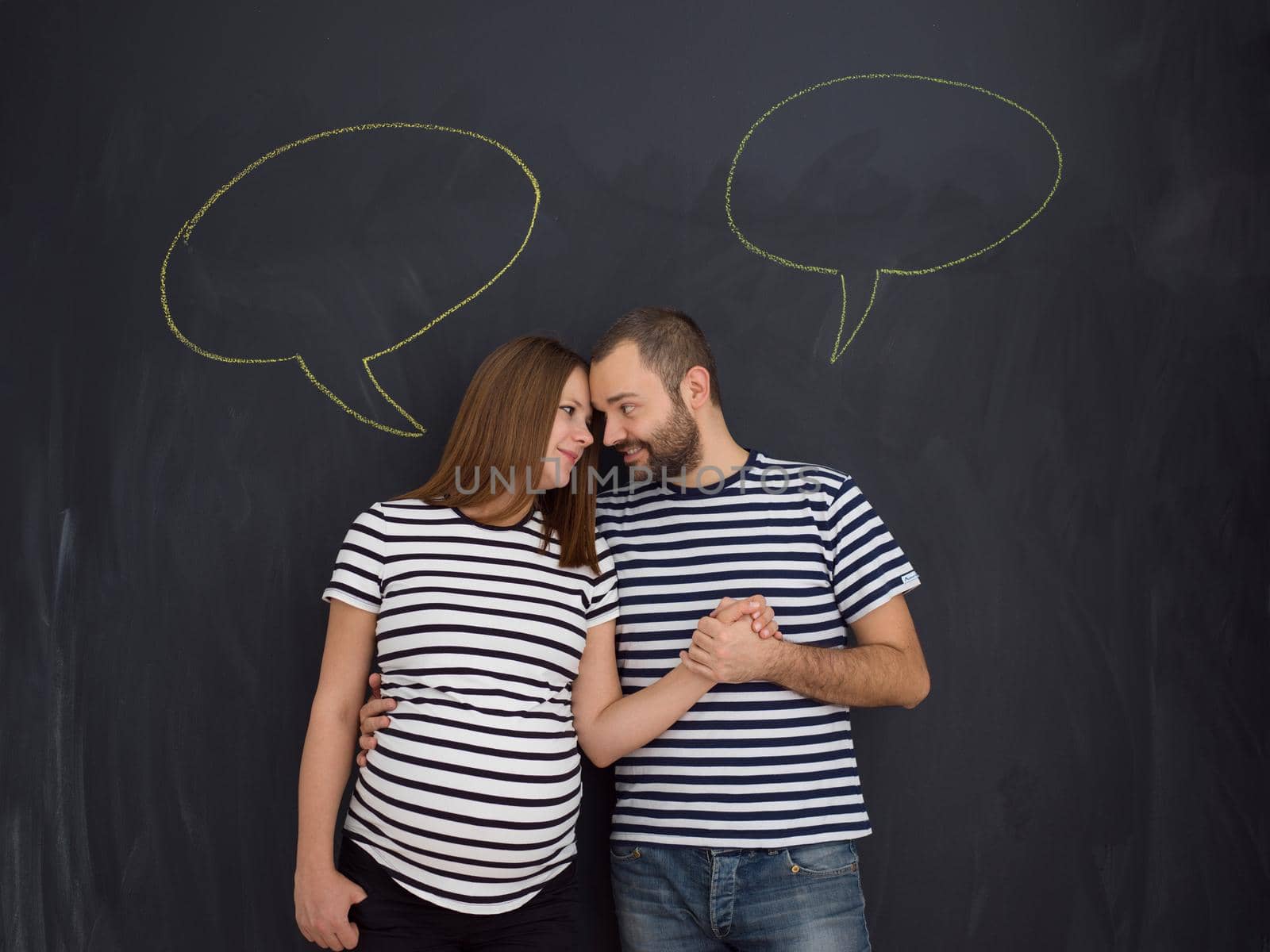 portrait of husband and pregnant wife posing against black chalk drawing board