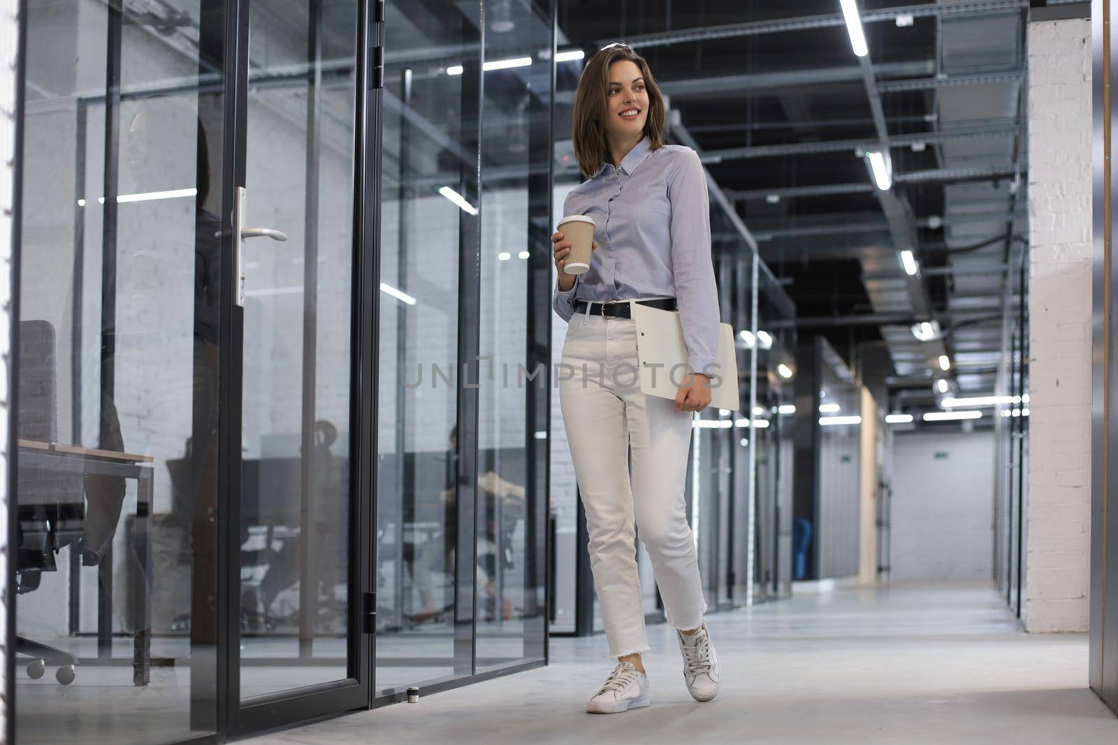 Businesswoman walking along the office corridor with documents