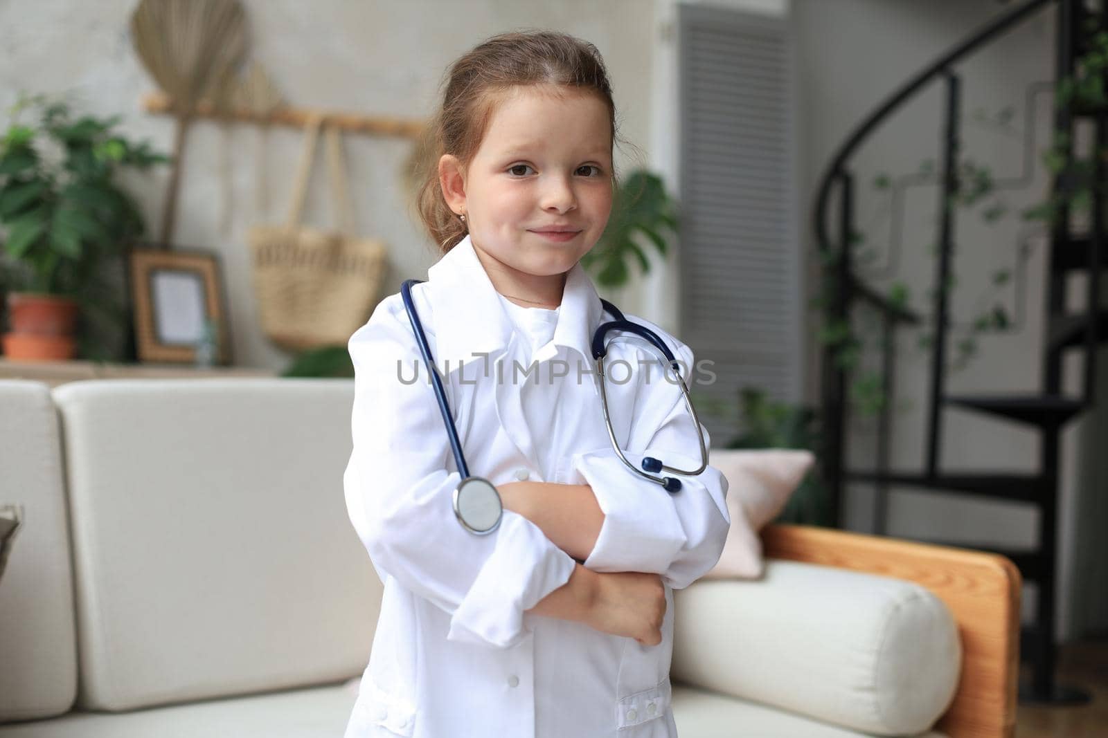 Smiling little girl in medical uniform playing with stethoscope at home