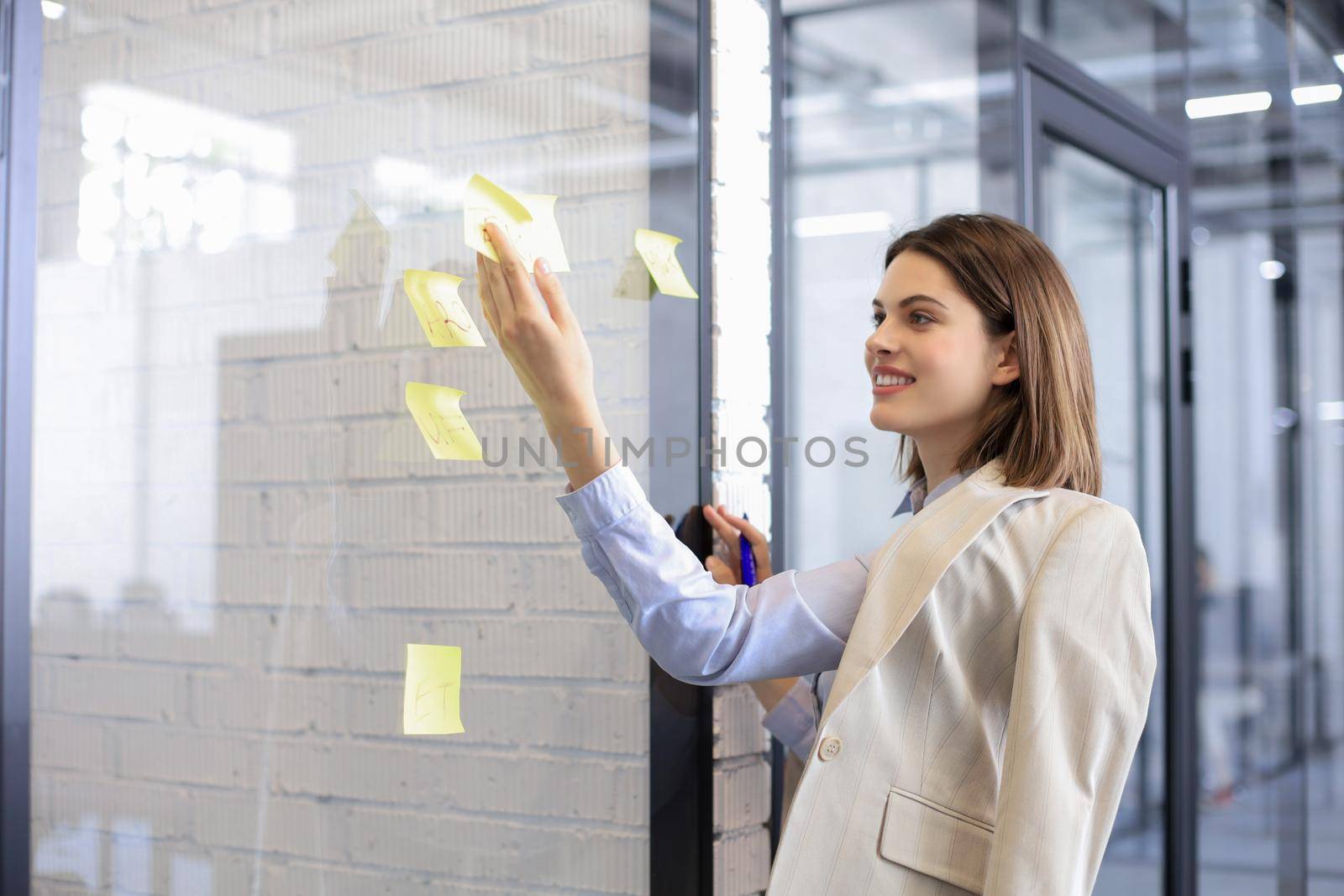 Attractive busness woman post stickers on glass at office and writing on them