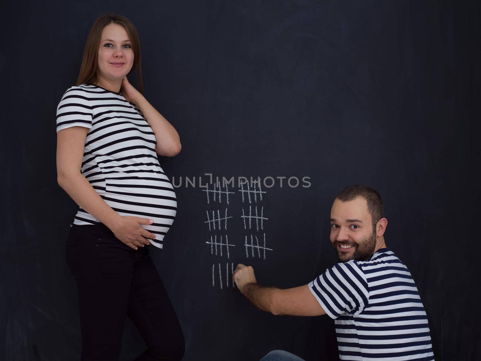 young pregnant couple accounts week of pregnancy and writing them with chalk on blackboard