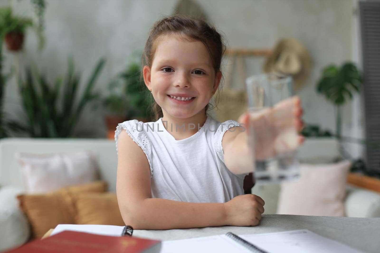 Happy little girl offer crystal still mineral water from glass, small child recommend daily dose of clean aqua