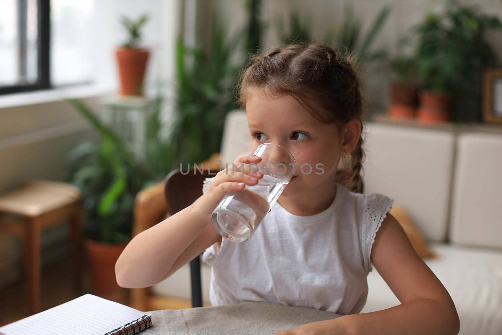 Happy little girl drinks crystal still mineral water in glass, small child recommend daily dose of clean aqua