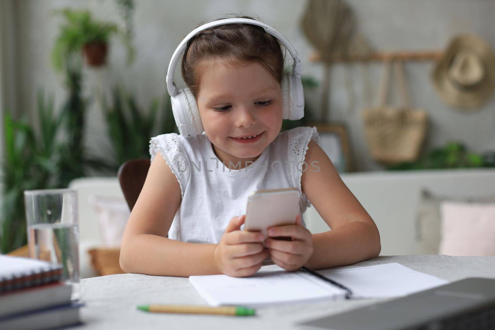 Smart little girl in headphones do homework online class on smartphone, small child in earphones study on Internet, have web conference or lesson during quarantine
