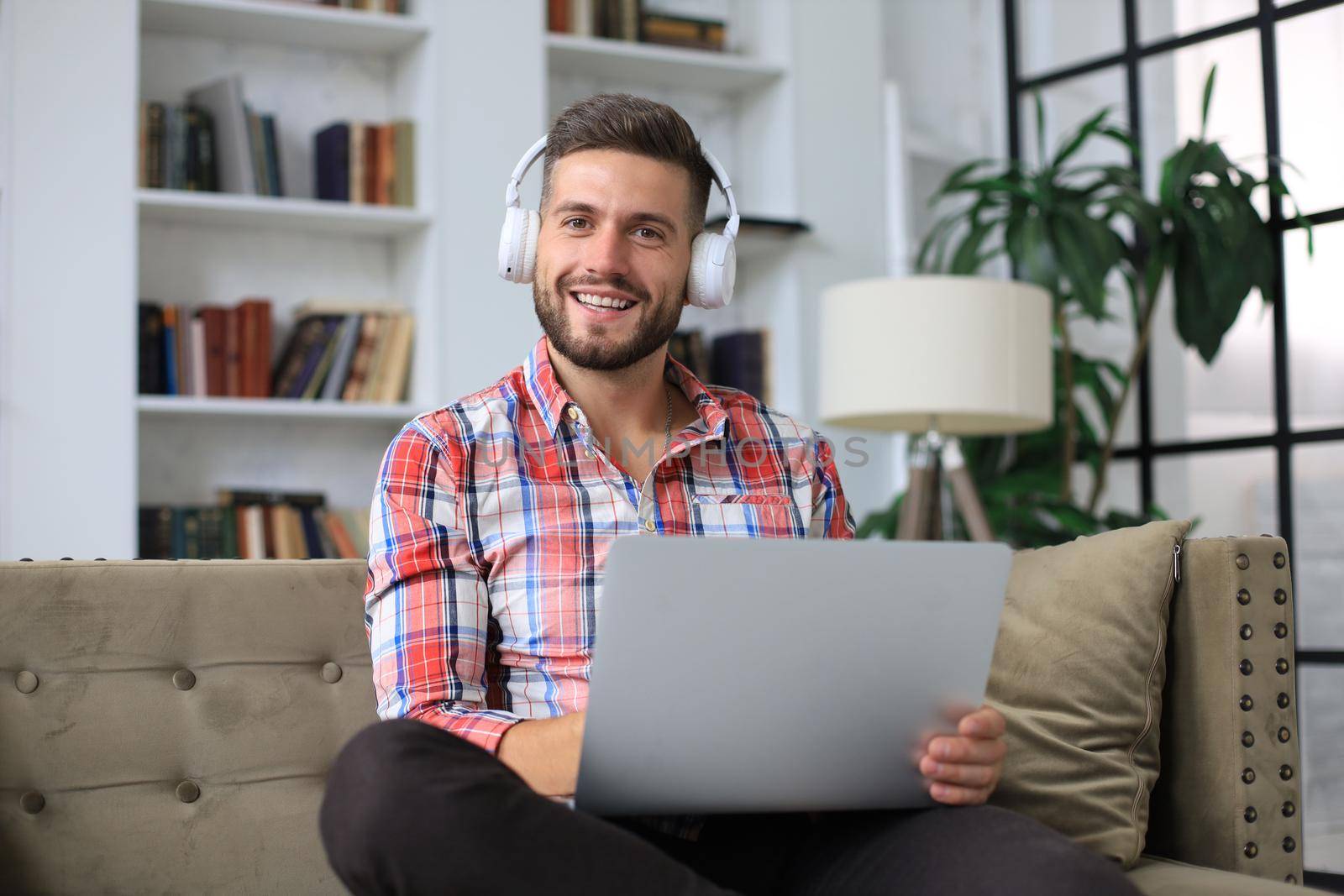 Concentrated young freelancer businessman sitting on sofa with laptop, working remotely online at home