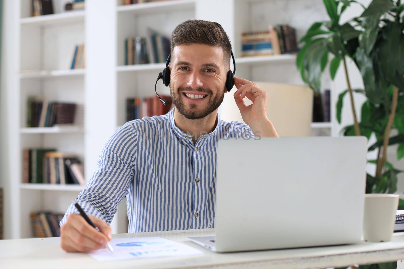 Thoughtful young business man writing something down while working in modern office