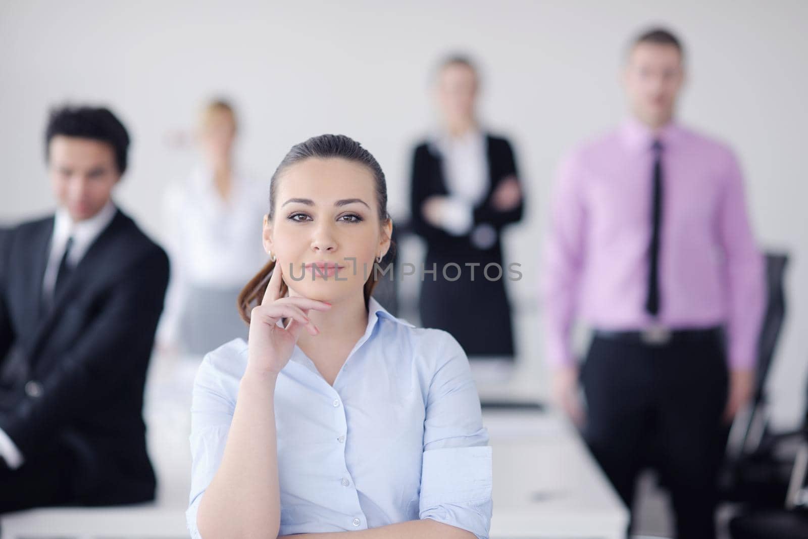 Successful business woman standing with her staff in background at modern bright office