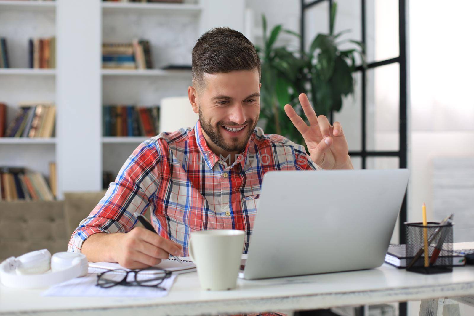 Smiling businessman greeting colleagues in video conference and negotiating distantly from home