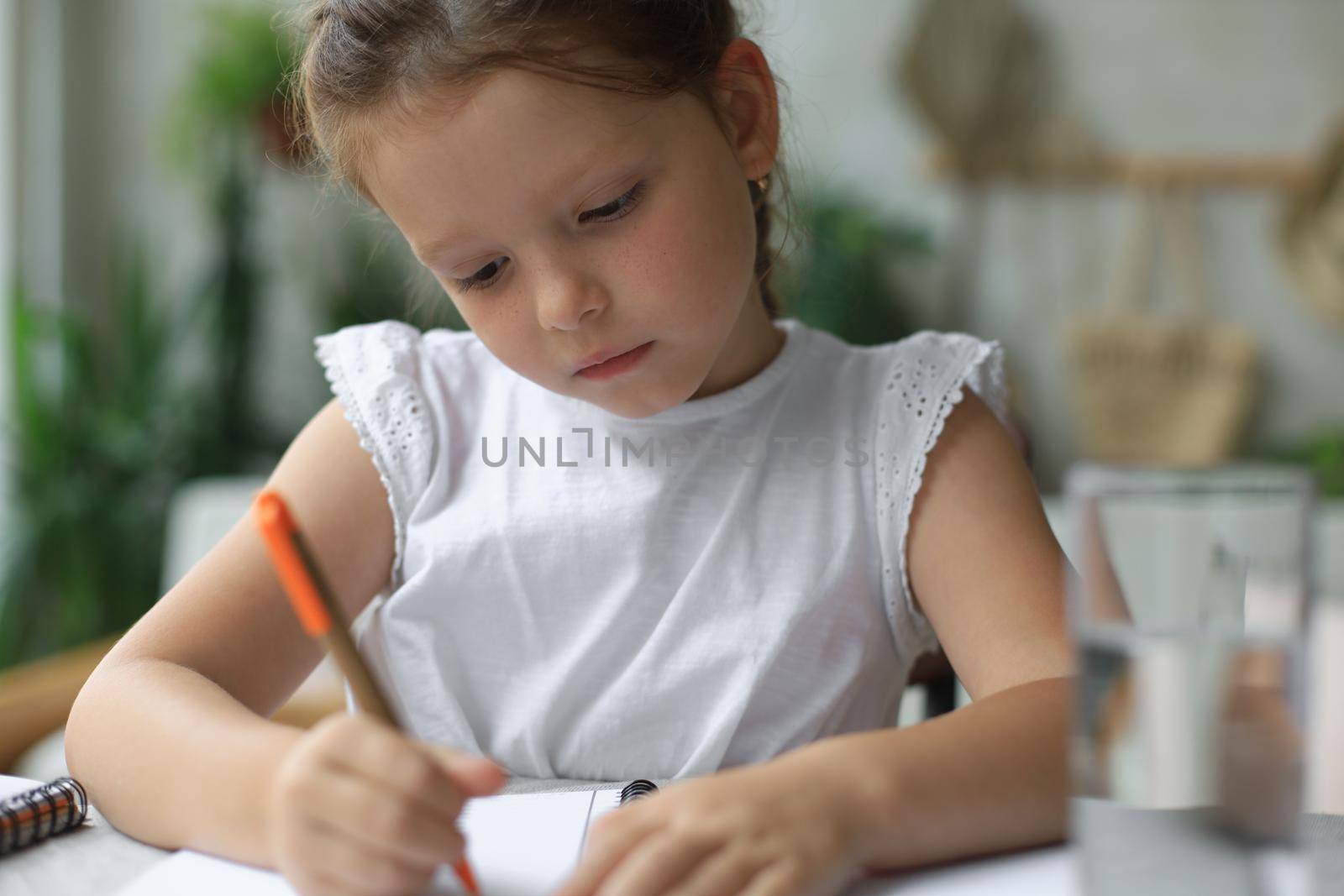 Little girl sit at desk, writing in notebook, do exercises at home, small child handwrite prepare homework