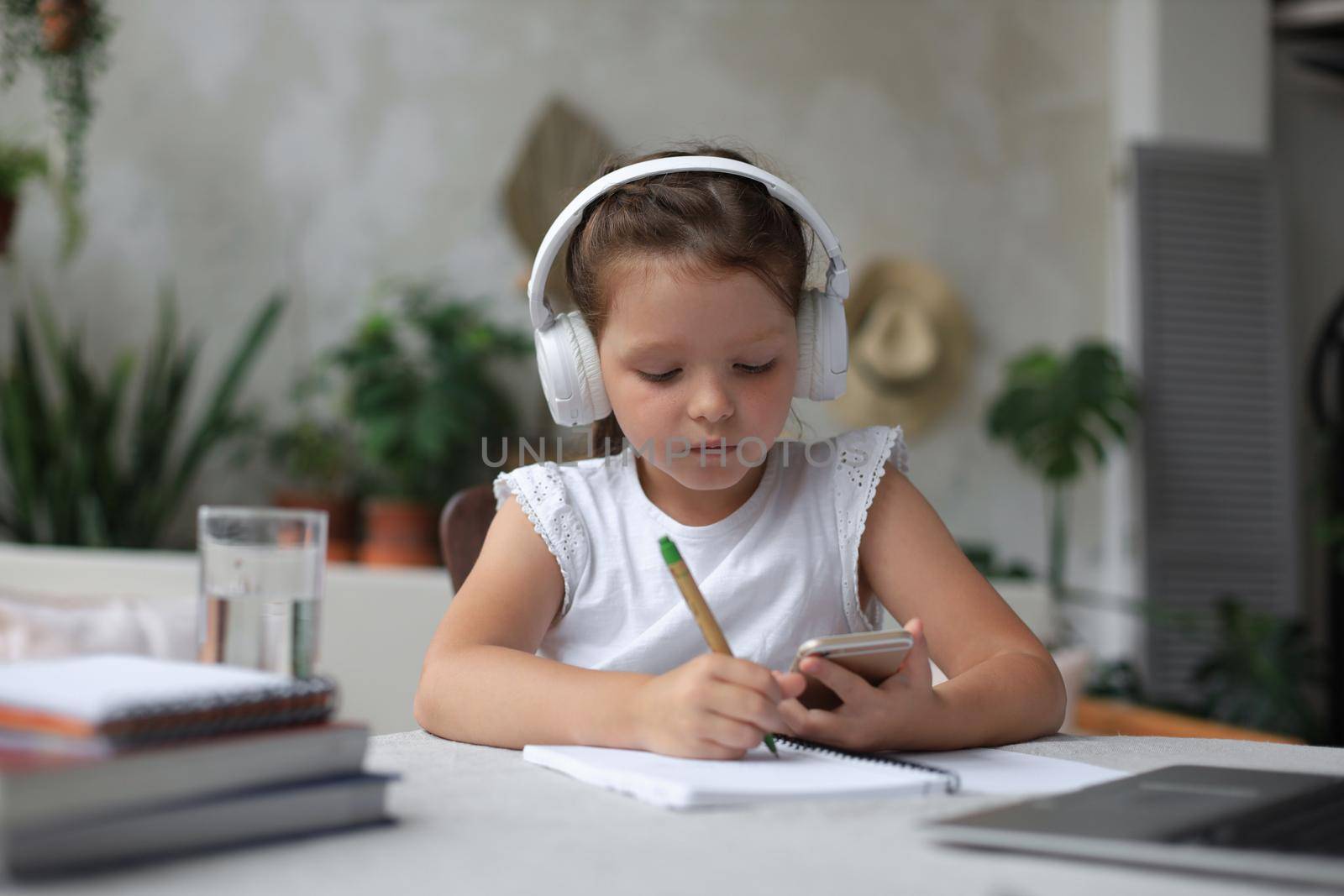 Smart little girl in headphones do homework online class on smartphone, small child in earphones study on Internet, have web conference or lesson during quarantine