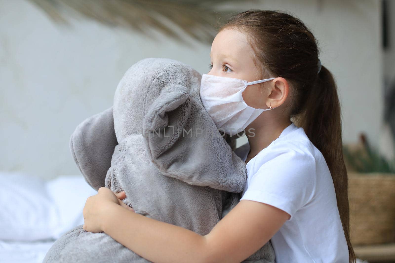 Stay at home quarantine coronavirus pandemic prevention. Sad child in protective medical mask and his elephant both in protective medical mask sit on bed