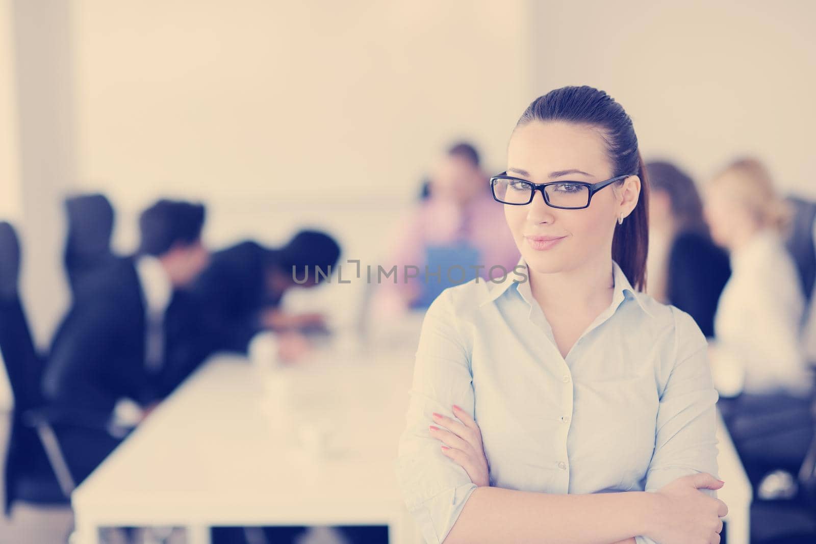 Successful business woman standing with her staff in background at modern bright office