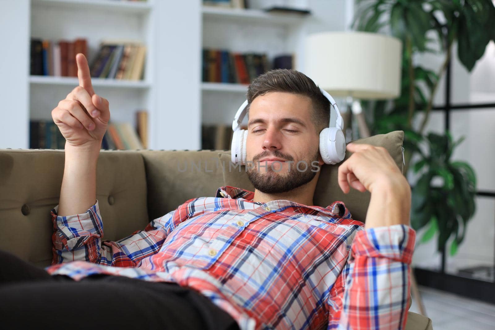 Young hipster man lies on the couch and listens to music in wireless headphones