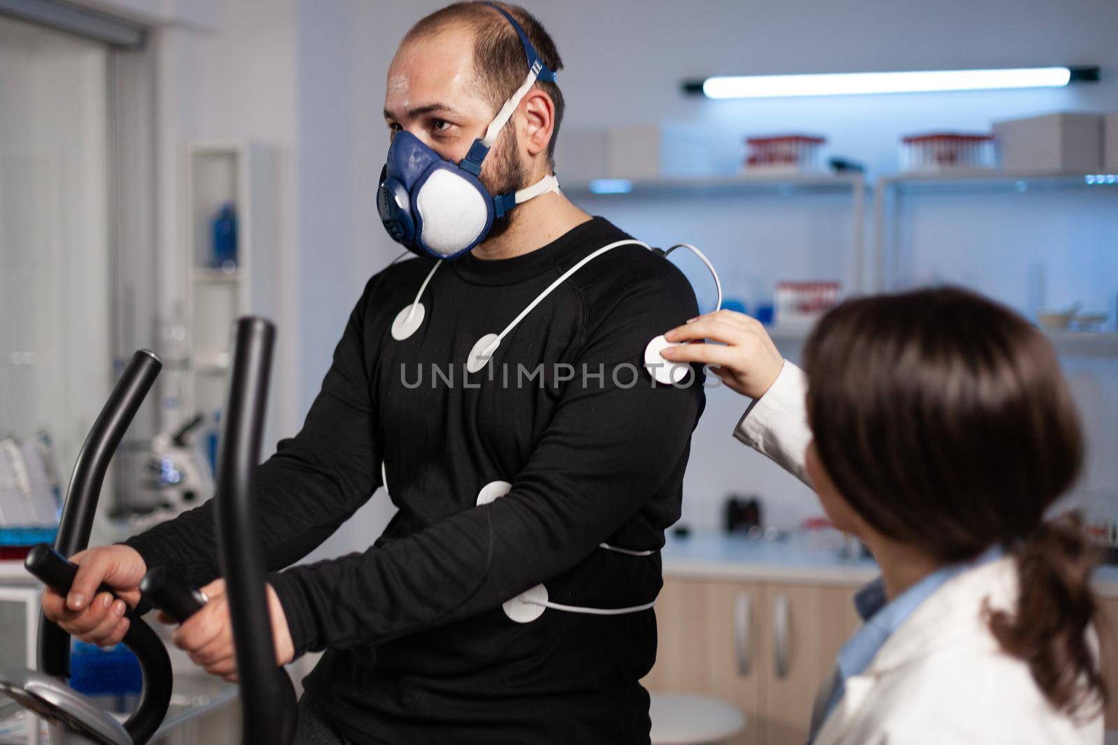 Specialist doctor physician putting electrodes sensor on sportman with mask monitoring EGK data in medical examination laboratory. Athlete man running on fintess trainer working at body endurance