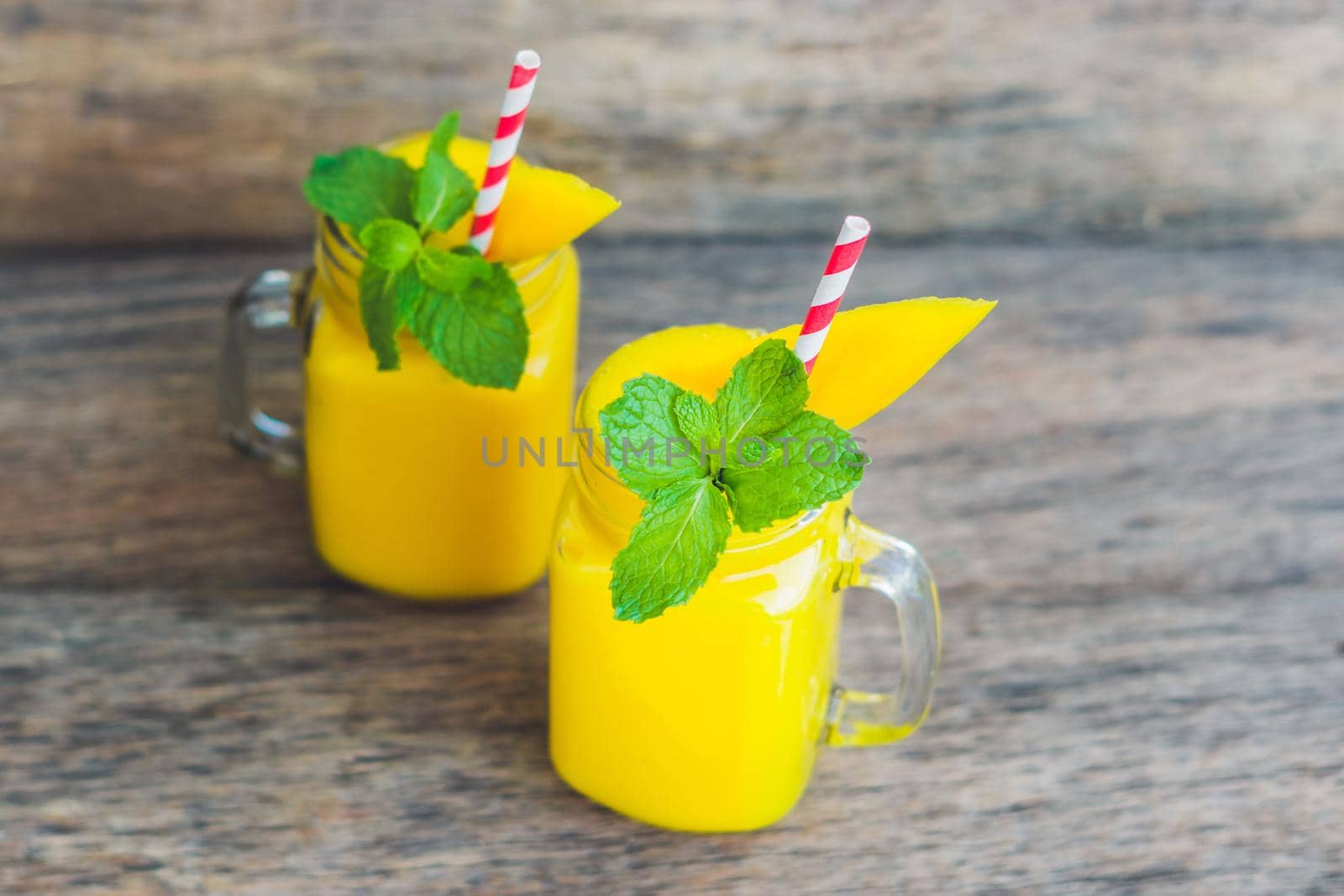 Juicy smoothie from mango in two glass mason jars with striped red straw on old wooden background. Healthy life concept, copy space by galitskaya