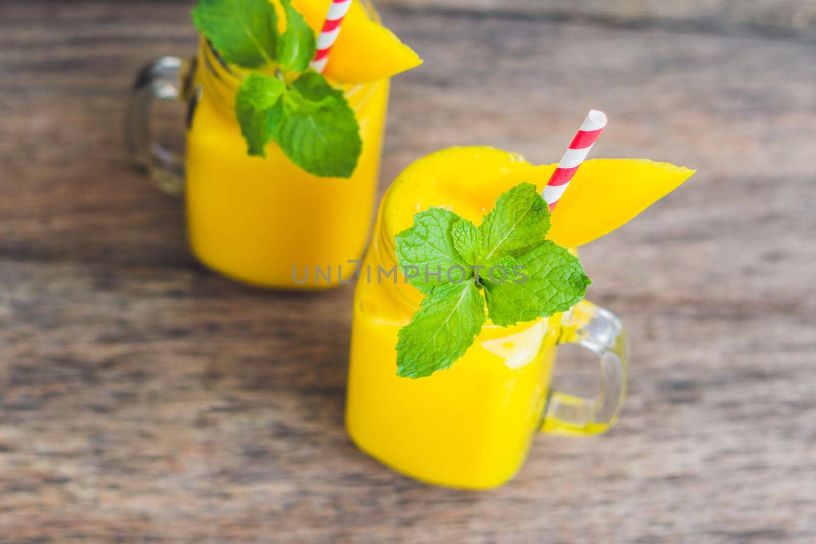 Juicy smoothie from mango in two glass mason jars with striped red straw on old wooden background. Healthy life concept, copy space by galitskaya