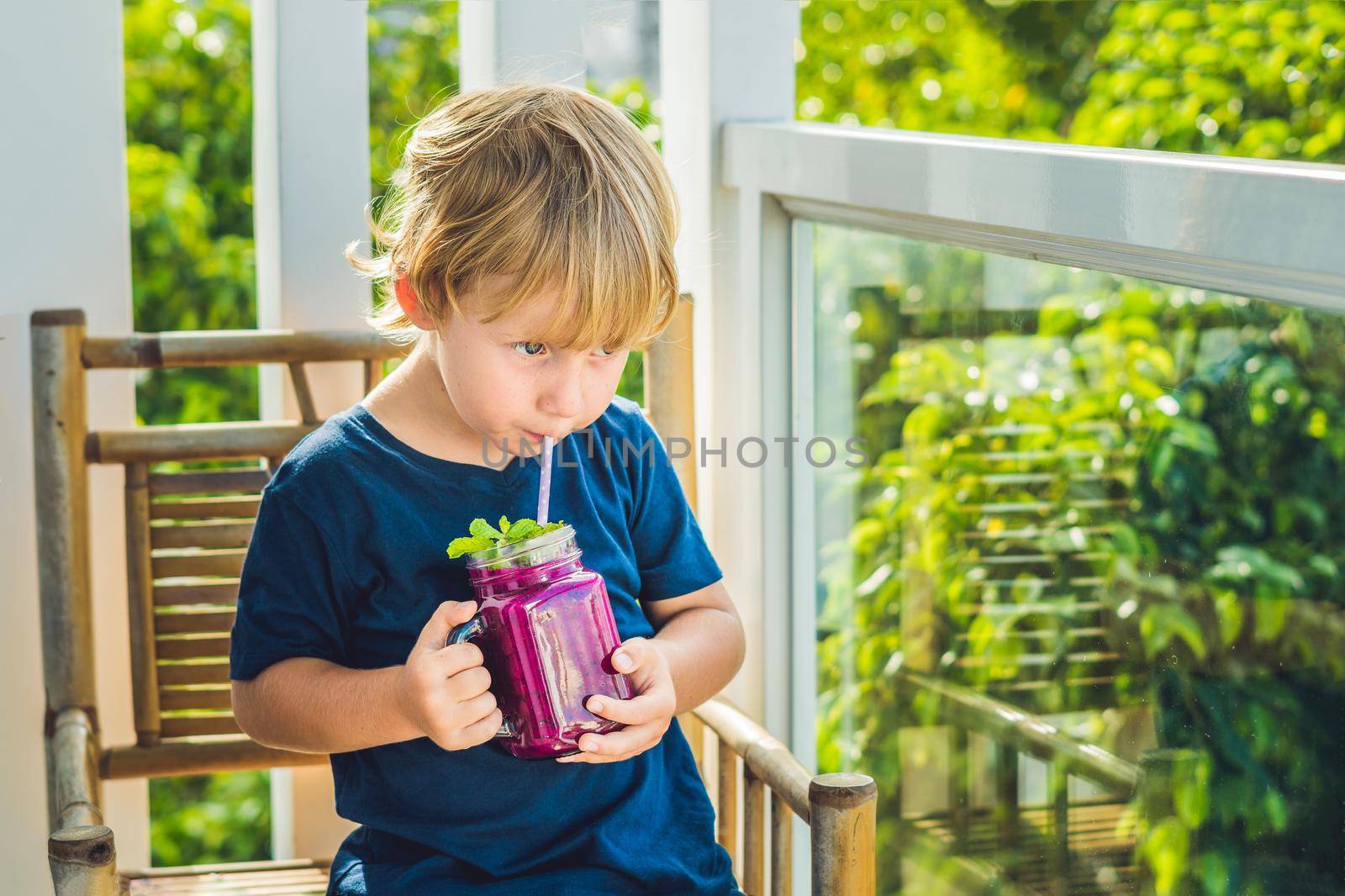 The boy holds smoothies from a dragon fruit with a mint leaf and a drinking straw.