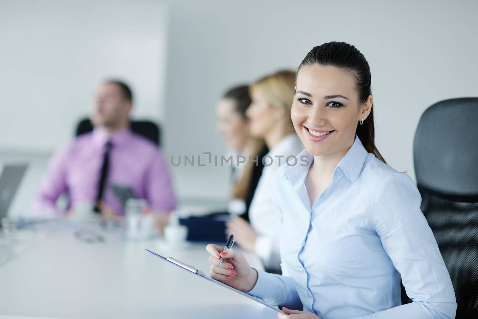 Successful business woman standing with her staff in background at modern bright office