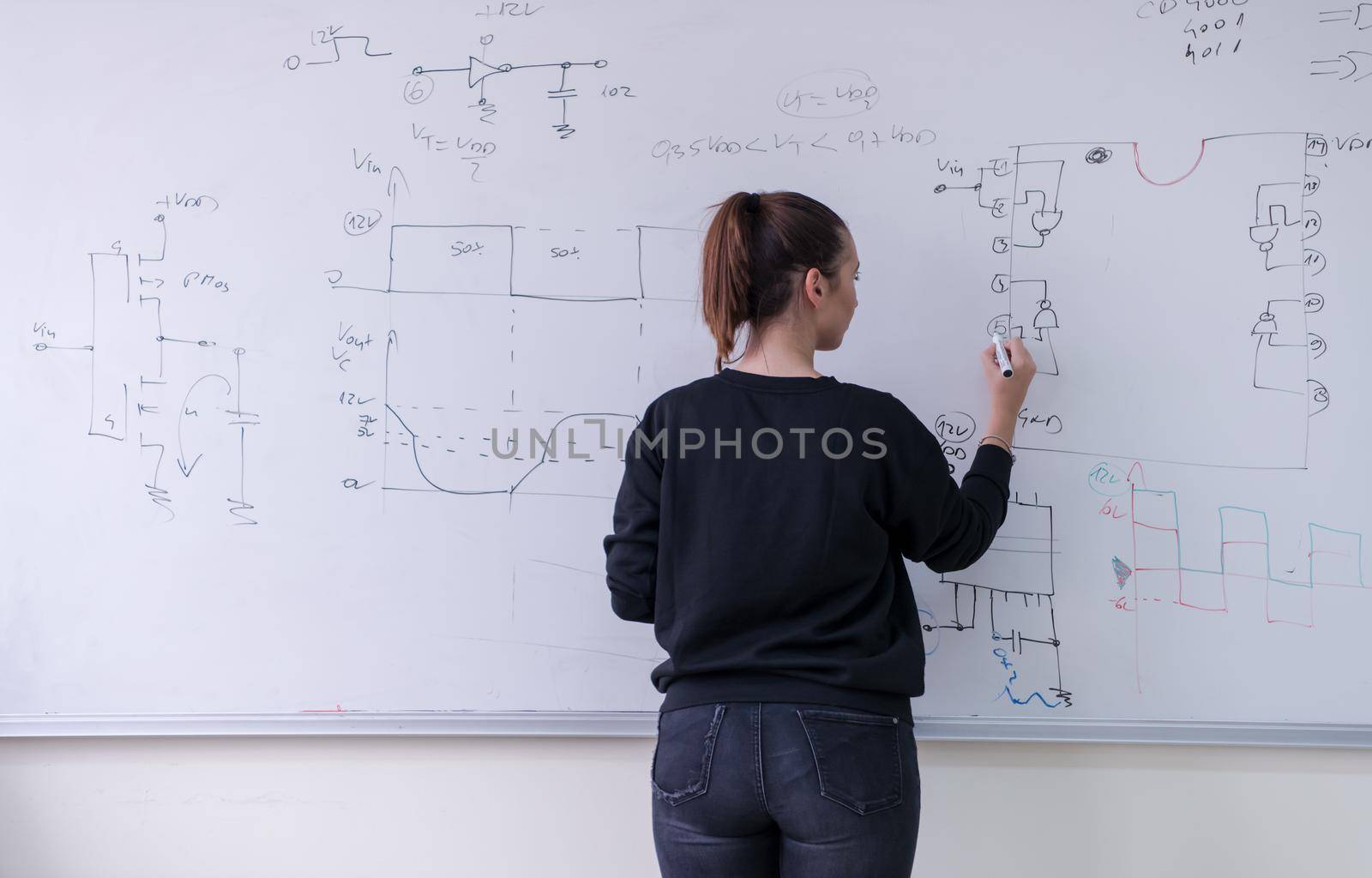 Young female student standing and writing on white chalkboard in a classroom