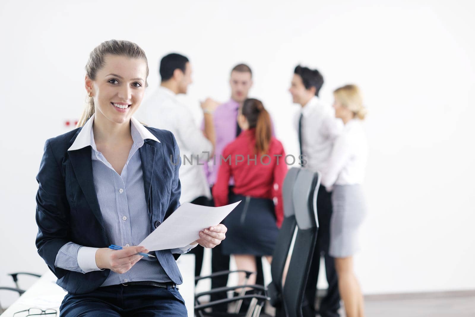 Successful business woman standing with her staff in background at modern bright office