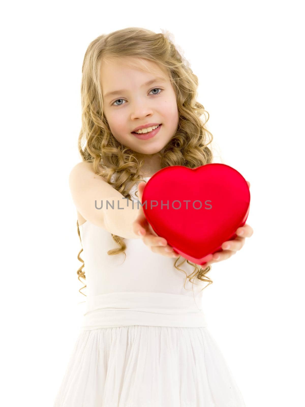 A cute little girl is smiling with a red heart at home. The concept of love, home, happiness and people.