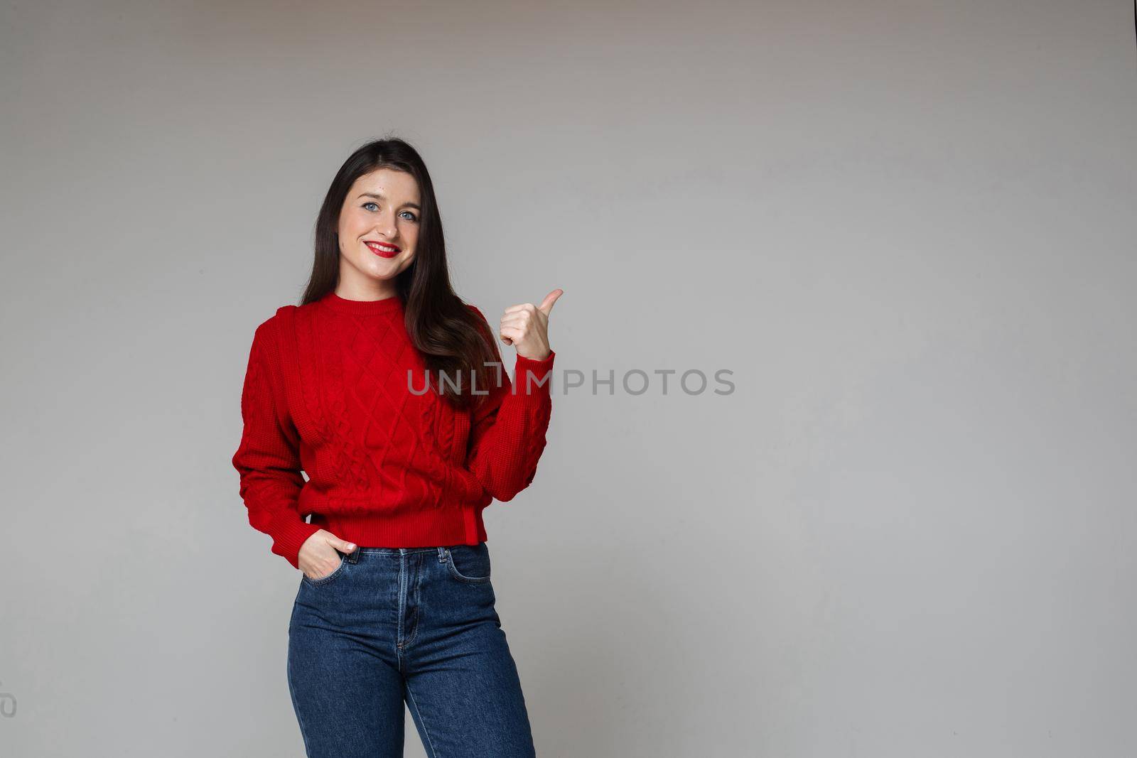 woman in warm red sweater and blue jeans keeps her hand in the pocket by StudioLucky