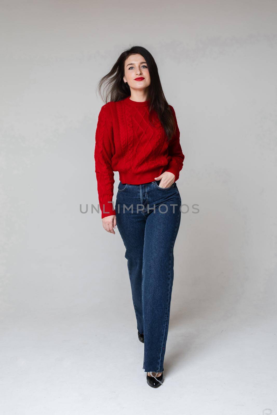 caucasian woman in red sweater and blue jeans keeps her hand in the pocket and walks by StudioLucky
