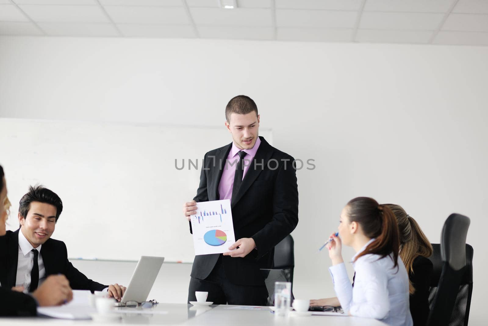 Group of young business people sitting in board room during meeting and discussing with paperwork