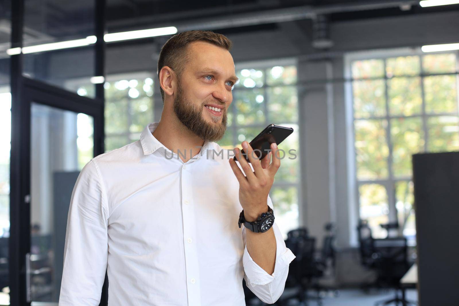 Handsome business man using a voice recognition app in office. by tsyhun