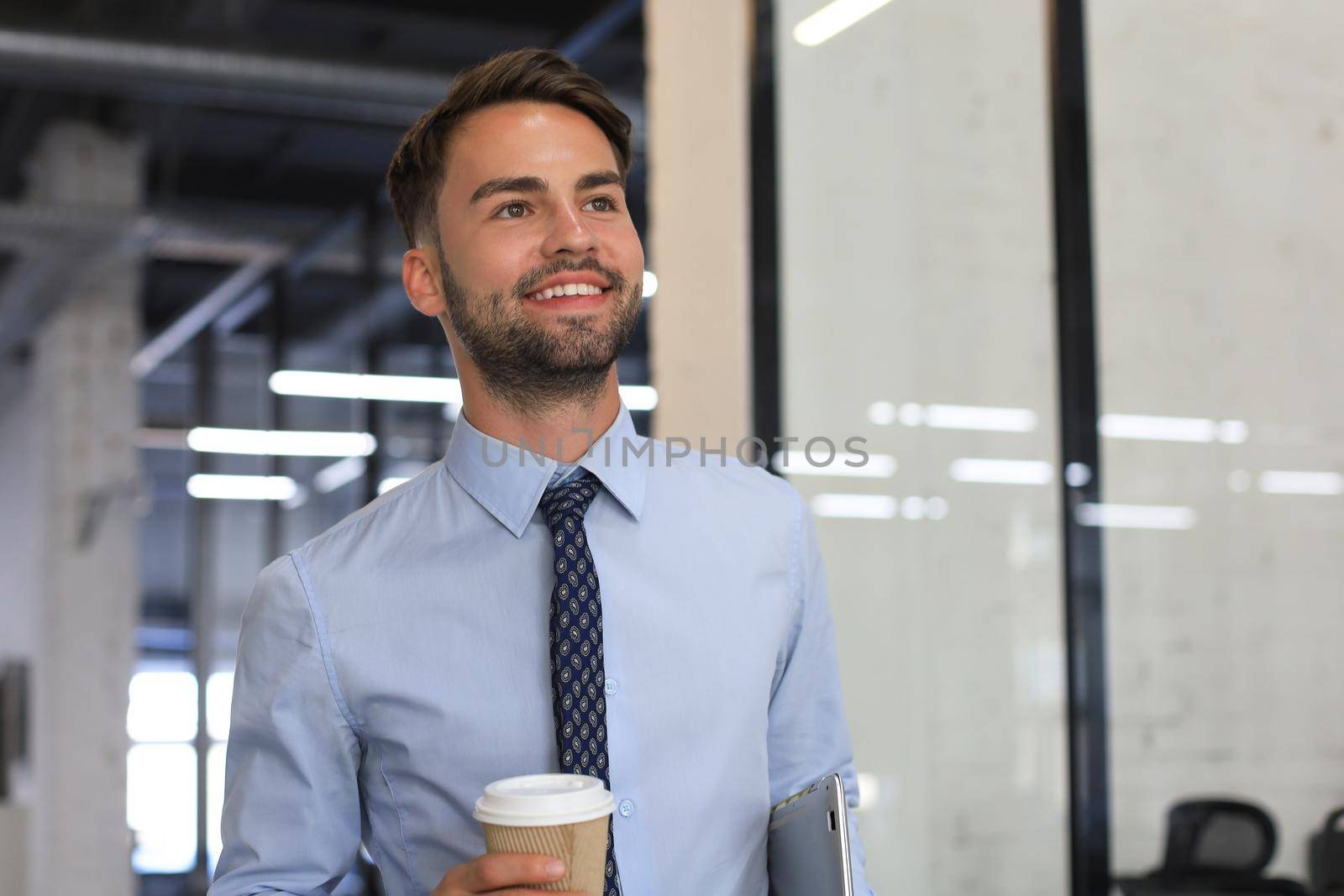 Businessman walking in office corridor with takeaway coffee