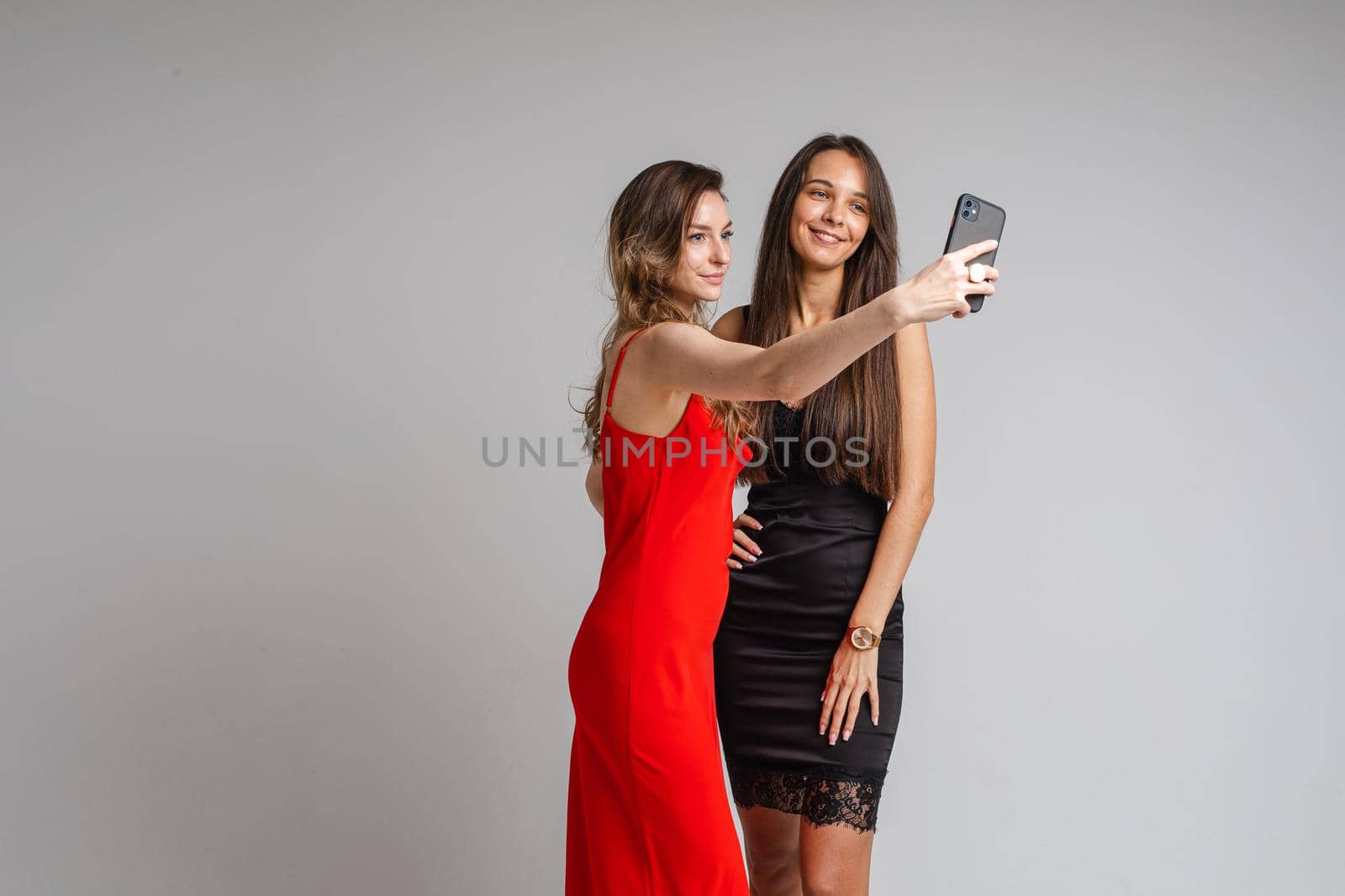 Pretty young girls bloggers wearing stylish dresses make selfie photography using phone posing on gray studio background. High quality photo