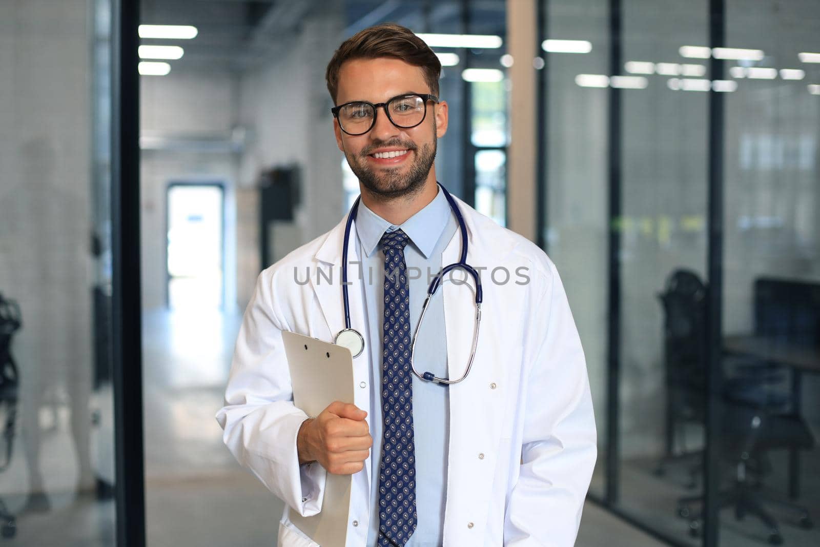 Handsome friendly young doctor on hospital corridor looking at camera, smiling