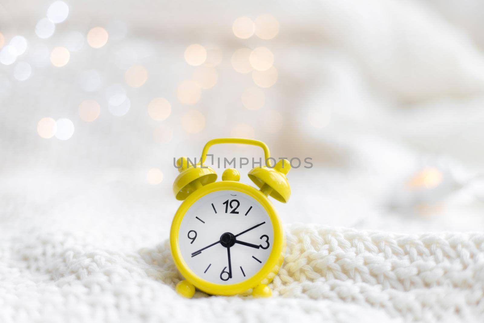 Alarm clock on a plaid with a garland . Yellow alarm clock. Cozy vibes . Home comfort. New Year and Christmas. Decorating