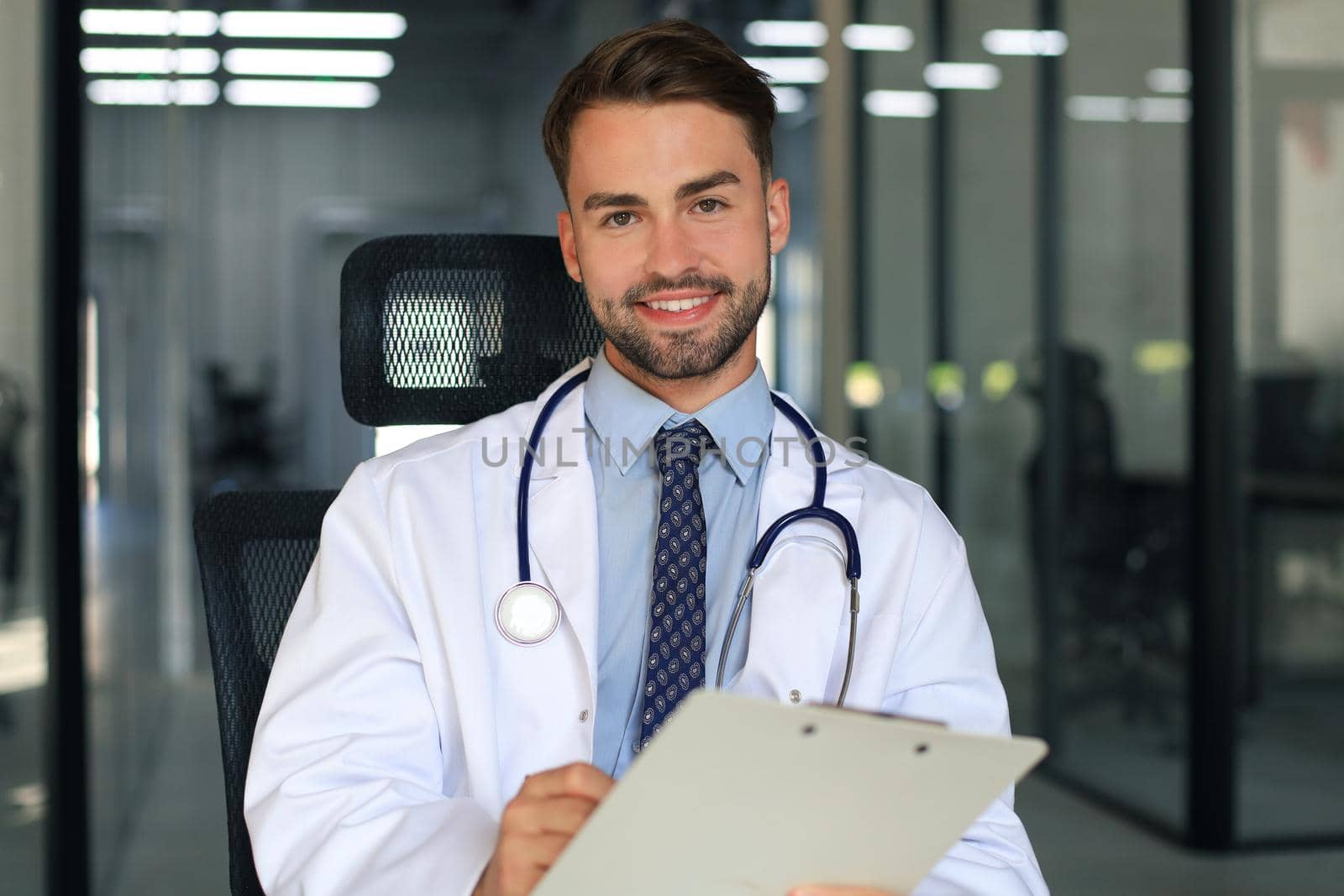 Handsome friendly young doctor on hospital corridor looking at camera, smiling