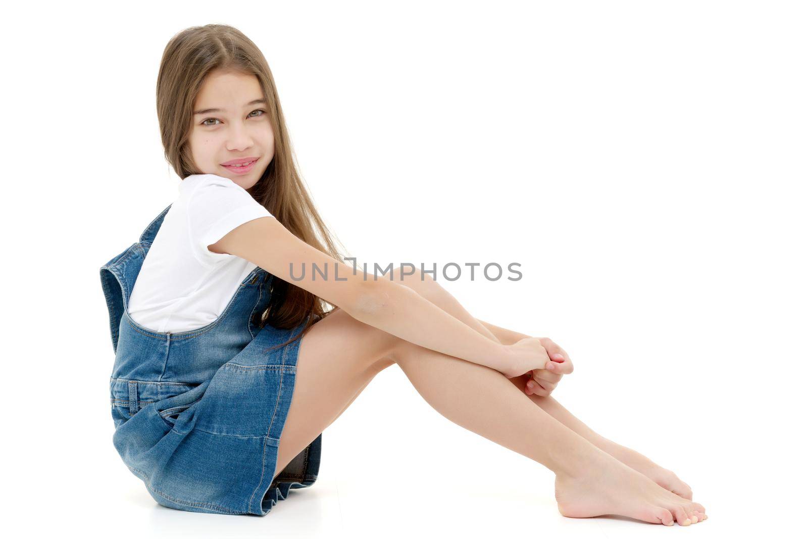 Cute girl posing on the floor in the studio. Hugs his knees. Isolated on white background. The concept of beauty and fashion